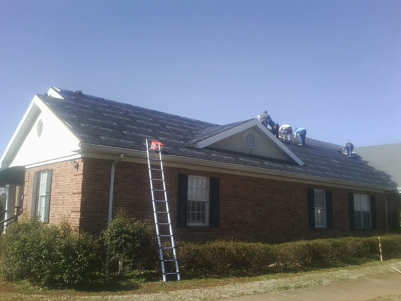 Crew tearing shingles off a brick ranch roof with a ladder set — Emergency Roof Repair work by our crew in Assonet