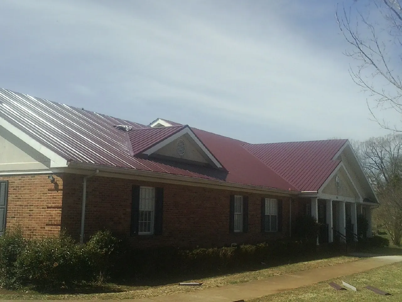 Red metal roof with gabled entries on a long brick building, from a Hail Damage Roof Repair job in Assonet
