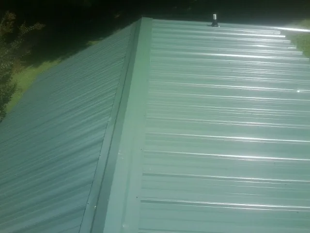 New green metal panels meeting at the ridge of a roof — Flat Roof Repair work by our crew in Assonet