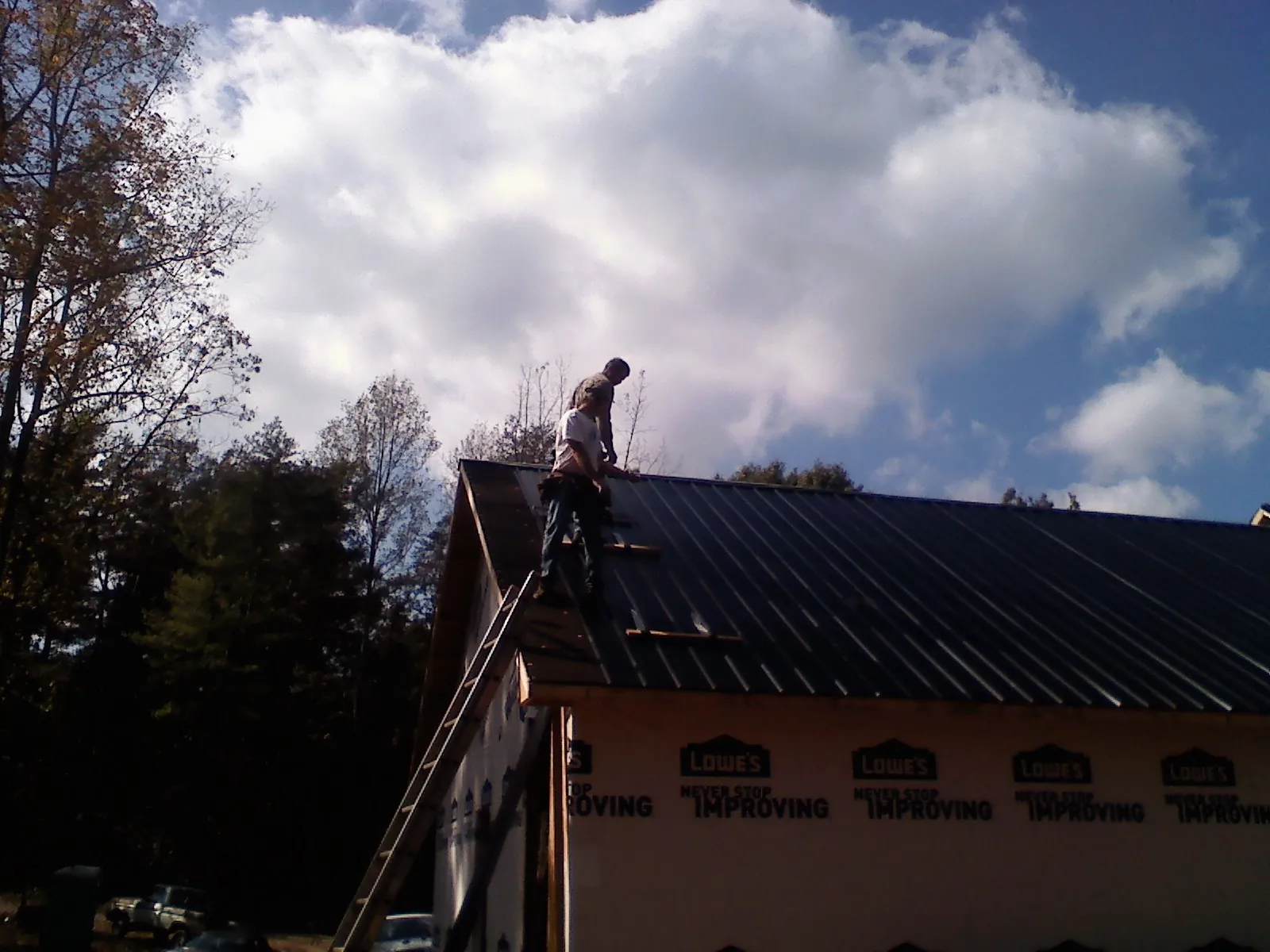 Roofer fastening dark metal panels high against a cloudy sky, from a Roof Inspection job in Assonet