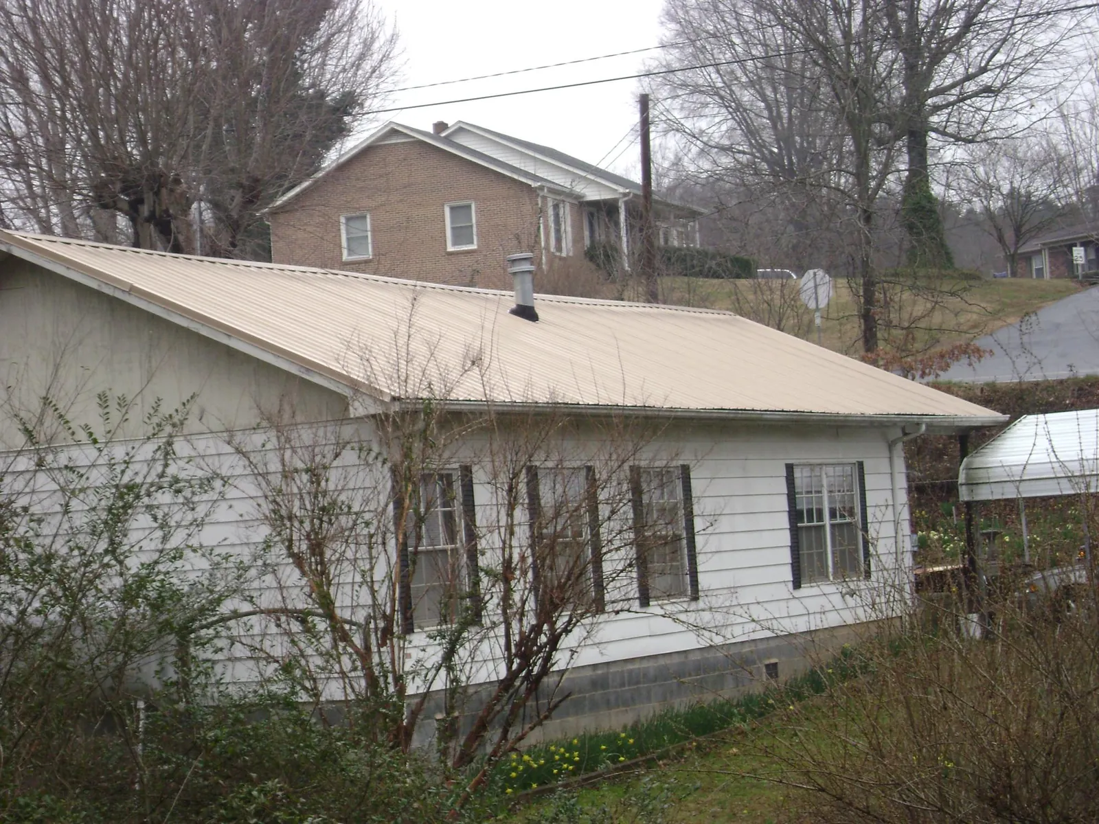Tan metal roof on a white sided house set into a hillside — Commercial Roofing by Roofing Brothers in Assonet